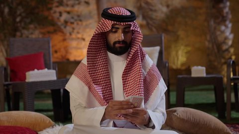 مفهوم التركيز والتحدي في لعب الشدة، تصوير لشاب عربي خليجي سعودي يرتدي الزي التقليدي و المشاغ يلعب لعبة الورق, مفهوم التركيز و التحدي, أنشطه ترفيهيه ممتعة, قضاء وقت ممتع فى الخارج