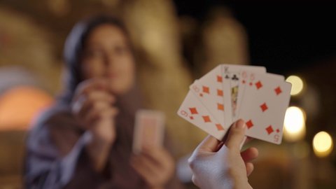 تعابير الفوز و الانتصار، ممارسة الأنشطة والألعاب الجماعية المسلية، التسلية والاستمتاع مع الأهل والأصدقاء في إحدى الشاليهات في العطلة الصيفية، مفهوم التركيز والتحدي في لعب الشدة، تصوير مقرب ليد امراة عربيه خليجيه سعودية تقوم بالعب لعبة الورق برفقه صديقتها