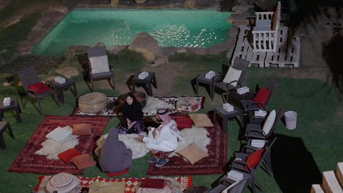 أجواء صيفية سعيدة، قضاء أوقات ممتعة في الهواء الطلق، التسلية والترفيه في إحدى الشاليهات السياحية،  تصوير لصديقتان عربيتان خليجيتان سعوديتان تجلسان مع صديقهم فى الخارج و يقومان بالدردشة و المناقشات