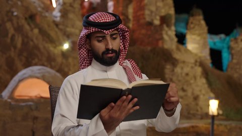 قضاء وقت الفراغ بالتعلم والثقافة، هواية المطالعة والاستكشاف، مفهوم التثقيف والبحث العلمي، رجل عربي خليجي سعودي يرتديالثوب الابيض و الشماغ يجلس فى الهواء الطلق و يقوم بقراءة كتاب