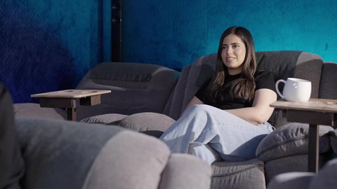 Enjoying drinks, a Saudi Gulf Arab family sitting in the cinema hall, expressions indicating happiness and engagement, spending enjoyable family time, watching movies and theatrical performances in the cinema, background of the cinema screening room, screening venues.