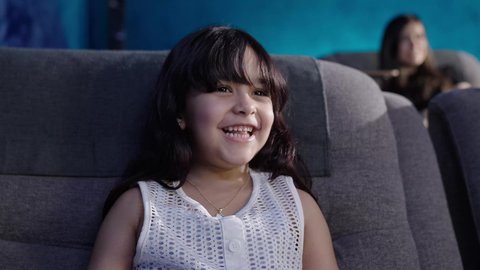 أنشطة عطلة نهاية الاسبوع،، تصوير مقرب لبنت عربية خليجية سعودية تجلس على كنبة مريحة تستمتع بمشاهده الافلام فى السينما، برامج ترفيهية للأطفال، ايماءات السعاده و السرور