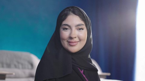 مفهوم الأنوثة والنعومة، الاهتمام بالمظهر الخارجي والأناقة، تصويرمقرب لامراة عربية خليجية سعودية تجلس بجوار نافذة مشرقة في غرفة مشمسة ترتدي الحجاب و العباءة السوداء ، النظرالى الكاميرا بايماءات السعادة و السرور