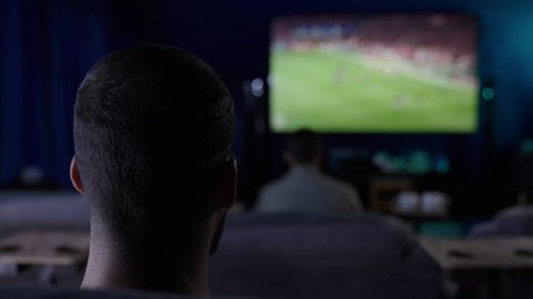 رفع اليدين الى الاعلى بتعابير الفوز، الانسجام والتفاعل مع المنافسة، التحدي والتشجيع والقوة, تعابيرالشغف والحماس بالفوز, تصوير من الخلف لشاب عربي سعودي خليجي يرتدي الثوب الابيض يقوم بمشاهدة المباريات والألعاب الرياضية، ايماءات الفرح والسرور والسعادة