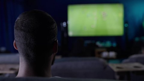 تعابيرالشغف والحماس بالفوز، التحدي والتشجيع والقوة, الانسجام والتفاعل مع المنافسة, رفع اليدين الى الاعلى بتعابير الفوز, تصوير من الخلف لشاب عربي سعودي خليجي يرتدي الثوب الابيض يقوم بمشاهدة المباريات والألعاب الرياضية، ايماءات الفرح والسرور والسعادة