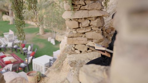 مفهوم الثقافة والاطلاع والتعلم الذاتي, إمرأة عربية خليجية سعودية ترتدي العباءة والحجاب تقوم بالقراءة والمطالعة في الهواء الطلق, الشغف بممارسة الهوايات المفيدة, الأنشطة الترفيهية الثقافية