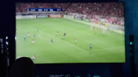 قضاء وقت الفراغ بمشاهدة التلفاز، ايماءات الحماس والسعادة والسرور، الانتصار و تحقيق الأهداف، امراة عربيه خليجيه سعوديه ترتدي العباءة السوداء تحمل بيديها كره القدم وتحتفل بفوز فريقها المفضل