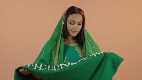 Pride in the nation's achievements, Saudi National Day September 23, Flag Day March 11, wearing the traditional costume of the central region on a national occasion, Badina Day February 22, close-up portrait of a Saudi Arabian Gulf woman wearing a sheila and bisht kissing the flag of the Kingdom, floral background