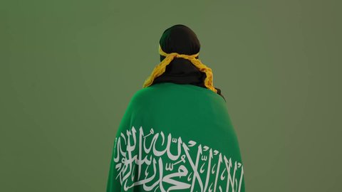 الاحتفال بذكرى اليوم الوطني السعودي 23 سبتمبر, يوم العلم 11 مارس، الاعتزاز بالتراث التاريخي، ارتداء زي المنطقة الوسطى، بورتريه من الخلف لإمرأة عربية خليجية سعودية مبتسمة ترتدي الكرتة والهامة تضع علم المملكة على كتفيها, خلفية خضراء، كروما