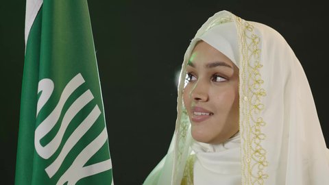 الاحتفال بالأعياد الوطنية، ارتداء أزياء المنطقة الشرقية، يوم العلم السعودي11 مارس، يوم بدينا 1727 م، بورتريه مقرب لإمرأة عربية خليجية سعودية ترتدي الشيلة والنشل تحمل علم يوم تأسيس الدولة السعودية الأولى، النظر إلى الكاميرا بتعابير الفخر، خلفية القمر المضيء ليلا