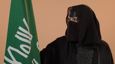 إظهار الولاء والحب للوطن, ذكرى تأسيس الدولة السعودية الأولى 1727م، بورتريه مقرب لامرأة عربية خليجية سعودية ترتدي البرقع والعباءة تحمل علم التأسيس تنظر إلى الكاميرا بإيماءات الاعتزاز والشموخ، الفخر بإنجازات المملكة، يوم بدينا 22 فبراير، خلفية زهري