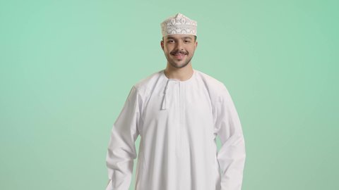 الاستفادة من الحسومات والتصفيات, متعة التسوق فى سلطنة عمان, التبضع وأخذ الحاجات الضرورية, أكياس الهدايا الورقية التجارية, بورتريه لشاب عربي خليجي عماني يرتدي الدشداشة و الكمة يمسك بيده حقائب المشتريات بايماءات بسعادة, خلفية خضراء