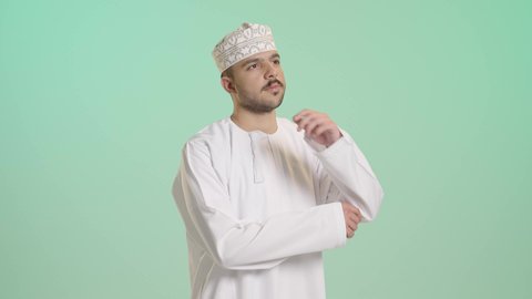 التمعن والتركيز لإيجاد حل لمشكلة، بورتريه مقرب عربي خليجي عماني يرتدي الدشداشة و الكمة يضع يده على ذقنه بتعابير التفكير والتركيز بشيء ما، ايماءات شرود الذهن والحيرة والقلق، التأمل و التخطيط للمستقبل، خلفية خضراء
