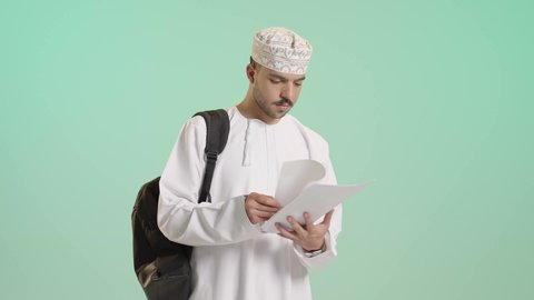 الاستعداد للعام الجامعي الجديد, الجامعات والكليات الأكاديمية في سلطنة عمان, بورتريه لطالب عربي خليجي عماني يرتدي الدشداشة والكمة يحمل حقيبة على ظهره يمسك بيده ورق يقوم بمتابعة الدروس اليومية, خلفية خضراء