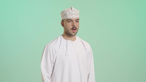 الشعور بالتعب والحاجة الى النوم والراحة, الإحساس بالكسل والخمول و الإرهاق، بورتريه لشاب عربي خليجي عماني يرتدي الدشداشة و الكمة يضع يده على فمه بإيماءات التثاؤب والنعاس، خلفية خضراء