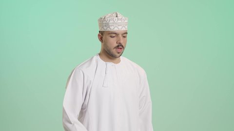 الشعور بالمرض و الكحة, الحاجة إلى زيارة الطبيب و العلاج, الإصابة بفايروس كورونا, الانفلونزا والتهاب الرئة, بورتريه لشاب عربي خليجي عماني يرتدي الدشداشة و الكمة يرفع يده إلى فمه بإيماءات السعال, خلفيه خضراء