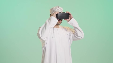 الاندماج ومحاكاة العالم الخيالي والنظر الى الافلام الواقعيه, التطور التقني والتكنولوجي, المتعة و التسلية بالمشاهدة عبر نظارة الواقع الافتراضي، بورتريه لشاب عربي خليجي عماني يرتدي الدشداشه والكمه ينظر من خلال نظارات ثلاثية الأبعاد (الفي ار)، خلفيه خضراء