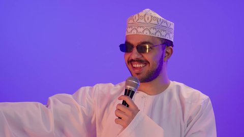 تقديم العروضات المسرحية, الفن المسرحي الغنائي, الغناء بحماس وصوت عالي، بورترية مقرب لشاب عربي خليجي عماني يرتدي الدشداشة و الكمه و النظارة الشمسية يقوم بممارسة هواية الغناء للتسلية والترفيه يحمل بيده الميكروفون، مواهب فنية في عالم الموسيقى، إيماءات وتعابير الاندماج و السعادة , خلفية بنفسجية