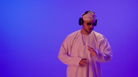 التفاعل مع الانغام الموسيقية, إيماءات وتعابير الاندماج مع الأغنية, مواهب غنائية فنية، بورتريه مقرب لرجل عربي خليجي عماني يرتدي الدشداشه والكمه و النظارة الشمسية يستمع الى الموسيقى من خلال سماعه الرأس، ايماءات تدل على الانصات والإستماع للأغاني بإستخدام الهيدفون، خلفية بنفسجية