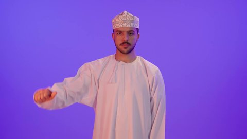 حركة يد وايماءات وجه تدل على عدم الإعجاب والموافقة، بورتريه لرجل عربي عماني يرتدي الدشداشة والكمه تظهر عليه علامات عدم القبول، الإشارة بإصبع الإبهام للاسفل دليل الرفض، خلفية بنفسجية