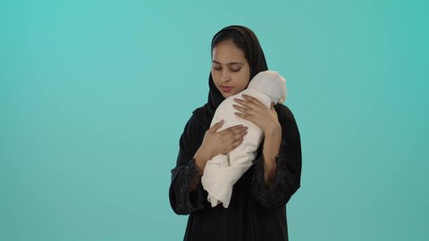 حنان الأمهات و رعاية الأبناء، الأسرة السعودية وتحمل المسؤولية، بورتريه لأم عربية خليجية سعودية محجبة تحمل رضيعتها بحب وحنان ، مفهوم الأمومة والطفولة، قضاء أوقات ممتعة بالعناية بالأطفال، خلفية خضراء