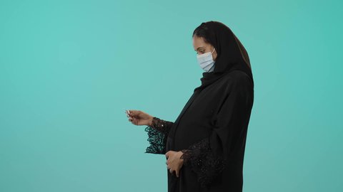 فحص طبي باستخدام الأشعة فوق الصوتية، مفهوم الحمل والأمومة، تصوير لامراة عربيه خليجيه سعودية محجبه ترتدي العباءة السوداء و الكمامة تقوم بعرض صورة أشعة لجنين، الوقاية من فايروس كورونا ، خلفية خضراء