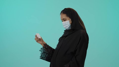 نتيجة فحص السونار الطبي، التشخيص الطبي عبر الأشعة الصوتية، مفهوم الحمل والأمومة، تصوير لامراة عربيه خليجيه سعودية محجبه ترتدي العباءة السوداء و الكمامة تقوم بعرض صورة أشعة لجنين، الوقاية من فايروس كورونا ، خلفية خضراء