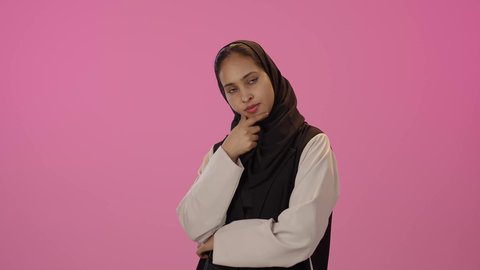 الشعور بالملل و شرود الذهن ، انتظار شيء ما ، بورتريه لشابة عربية خليجية سعودية سمراء ترتدي  الزي الكاجوال و الحجاب تضع يدها على ذقنها بإيماءات التمعن فى حل مشكلة، النظر الى شئ ما بتعابير التركيز، خلفية ملونه