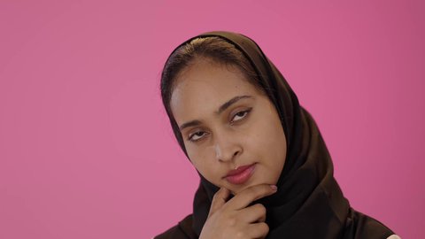 انتظار شيء ما ، الشعور بالملل و شرود الذهن ، بورتريه مقرب لشابة عربية خليجية سعودية سمراء ترتدي الزي الكاجوال و الحجاب تضع يدها على ذقنها بإيماءات التمعن فى حل مشكلة، النظر الى شئ ما بتعابير التركيز، خلفية ملونه