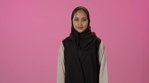 Facial expressions and body language indicating an excellent state, looking at the camera with happiness and joy, a sign of quality and perfection, a close-up portrait of a young Arab Gulf Saudi woman with a dark complexion wearing a hijab and casual attire, gesturing with signs of acceptance and excellence, colorful background.