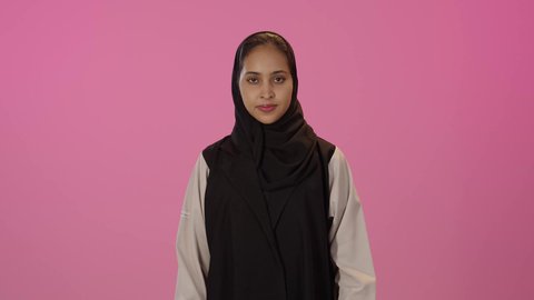 تعابير الإعجاب والرضى، النظر الى الكاميرا بتعابير السرور, علامة الجودة و الامتياز،  بورتريه لشابة عربية خليجية سعودية سمراء مبتسمة محجبة ترتدي الزي الكاجوال ترفع اصبع الابهام للاعلى بإيماءات القبول و الموافقة، خلفية ملونه