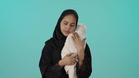 الشعور بالأمان والاطمئنان، تعزيز رابط الأمومة بين الأم وصغيرتها، مفهوم حنان الأمهات و تحمل المسؤولية والعناية بالأطفال، بورتريه مقرب لسيدة عربية خليجية سعودية سمراء  تحمل طفلتها الرضيعة بحب، خلفية خضراء