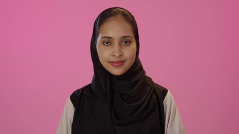 النظر الى الكاميرا بتعابير السرور, علامة الجودة و الامتياز،  بورتريه لشابة عربية خليجية سعودية سمراء مبتسمة محجبة ترتدي الزي الكاجوال ترفع اصبع الابهام للاعلى بإيماءات القبول و الموافقة، خلفية ملونه