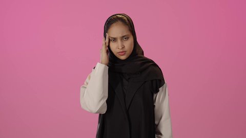 الحاجة إلى العلاج والمساعده، المعاناة من آلام الشقيقة، الشعور بألم الرأس والصداع، الحاجة للهدوء والراحة، بورتريه لشابة خليجية سعودية سمراء محجبة ترتدي الزي الكاجوال  تضع يديها على رأسها بايماءات التعب والارهاق، خلفية ملونه