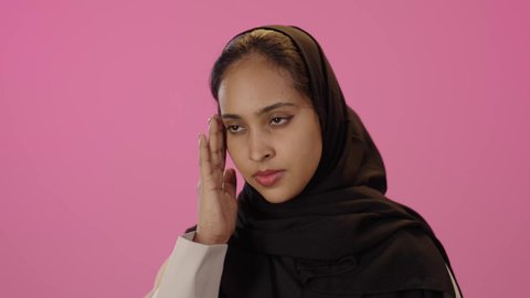 المعاناة من آلام الشقيقة، الحاجة إلى العلاج والمساعده، الشعور بألم الرأس والصداع، الحاجة للهدوء والراحة، بورتريه مقرب لشابة خليجية سعودية سمراء محجبة ترتدي الزي الكاجوال تضع يديها على رأسها بايماءات التعب والارهاق، خلفية ملونه