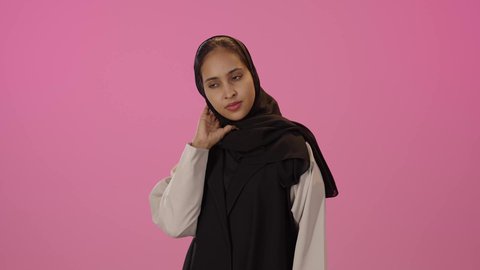 الم واوجاع الرقبه، بورترية لشابة عربيه خليجيه سعودية سمراء ترتدي الحجاب و الزي الكاجوال تضع يدها على رقبتها بايماءات التعب والارهاق، آلام الرقبه والعمود الفقري، اثار الشد العضلي، تعابير التعب والارهاق, الحاجه الى العلاج، خلفية ملونه