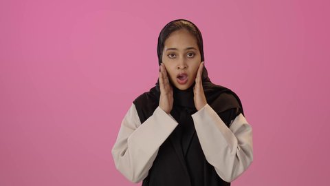 إيماءات الذهول والاستغراب، الوقوف باستقامة والنظر إلى الكاميرا، مفهوم النعومة والانوثة والاناقة، بورتريه لإمرأة عربية سعودية خليجية محجبة سمراء ترتدي الزي الكاجوال ترفع يديها نحو الأعلى بتعابير الدهشة، خلفية ملونه