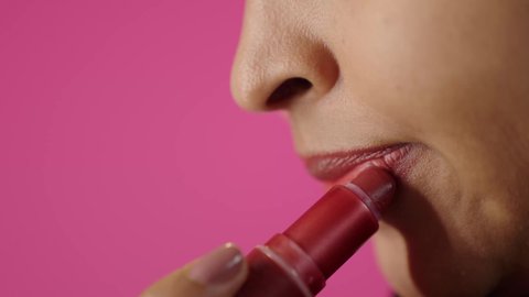 مفهوم الاهتمام بالجمال والمظهر الخارجي، مستحضر تجميلي نسائي, جودة المنتج السعودي, أدوات مكياج تتوريال, بورتريه مقرب لأيدي امرأة عربية سعودية خليجية سمراء تقوم بوضع أحمر الشفاه, خلفية ملونه