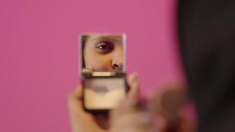 الاستمتاع بوضع الميك اب، الاهتمام بالجمال والمظهر الخارجي, التسويق لمساحيق التجميل, مفهوم التزين والتجمل, بورتريه مقرب لامرأة عربية خليجية سعودية سمراء محجبة ترتدي العباءة تقوم باستخدام فرشاة أحمر الخدود، خلفية ملونه