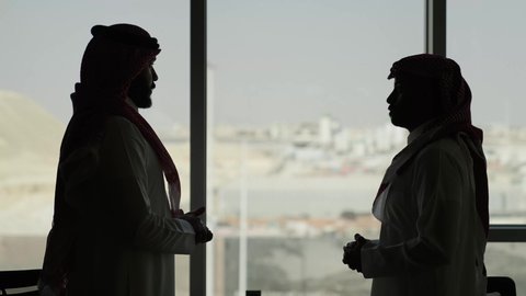 تبادل النقاشات في مهام العمل, مهنة ووظيفة سعوديه, بيئة مريحة في الشركات السعوديه, شرح خطط و استراتيجيات المهام المطلوبة, التعارف وبناء العلاقات الاجتماعية, رجل أعمال عربي خليجي سعودي خليجي يرتدي الثوب التقليدي والشماغ مع موظف يجلس داخل مقر الشركة