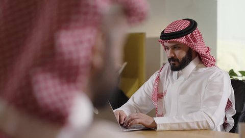 دراسه المشروع ومراجعه التقرير السنوي، استخدام التقنيات الحديثة المتطورة، جلسه عمل عن بعد, أداء المهمة اليومية داخل مقر الشركه، رجل أعمال عربي خليجي سعودي يرتدي الثوب التقليدي والشماغ يقوم بالعمل على جهاز الحاسوب المكتبي، دمج التقنية والتكنولوجيا في الحياة العملية