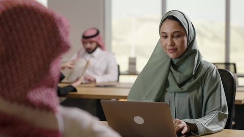 استخدام التقنيات الحديثة المتطورة، دراسه المشروع ومراجعه التقرير السنوي،جلسه عمل عن بعد, أداء المهمة اليومية داخل مقر الشركه، امراة عربية خليجية سعودية محجبة ترتدي العباءة الملونة تقوم بالعمل على جهاز الحاسوب المكتبي، دمج التقنية والتكنولوجيا في الحياة العملية