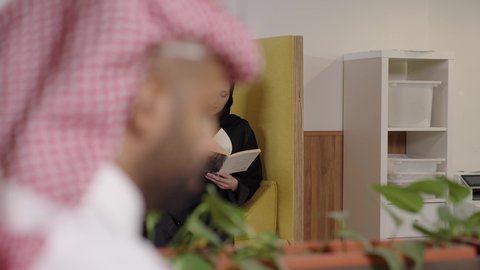 ممارسة هواية المطالعة, أماكن هادئة مريحة للدراسة، مفهوم الشغف بالقراءة, امراة عربية خليجية سعودية محجبة ترتدي العباءة الملونة تمسك كتاب بيديها, الكتب و الروايات على المسلية