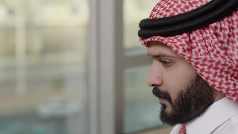 دراسه المشروع ومراجعه التقرير السنوي، جلسه عمل عن بعد، تصوير مقرب لرجل أعمال عربي خليجي سعودي يرتدي الثوب التقليدي والشماغ يقوم بالعمل على جهاز الحاسوب المحمول داخل مقر الشركه، دمج التقنية والتكنولوجيا في الحياة العملية، أداء المهمة اليومية داخل مقر الشركه