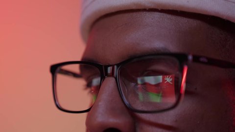A close-up of the eye of a dark-skinned Omani Gulf Arab man wearing glasses, looking proudly at the flag of the Sultanate of Oman, the reflection of the Omani flag on the lens of the glasses, commemorating Independence Day and Founding Day, November 18