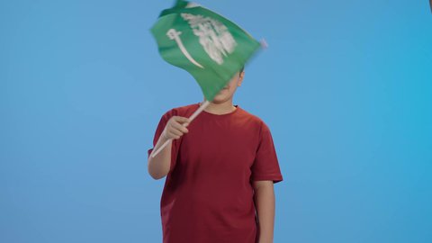 بورتريه لولد عربي خليجي سعودي يمسك بيده علم المملكة العربية السعودية ، ذكرى اليوم الوطني السعودي ،الاحتفال بالعيد الوطني السعودي