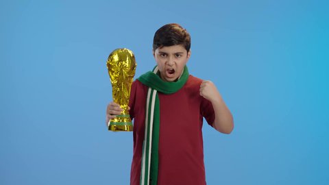 الشغف بالانشطة الترفيهية، المباريات والالعاب الرياضية,  التفاعل والاندماج بمشاهدة الفريق المفضل,ايماءات الفرح والحماس ,بورتريه لولد عربي سعودي خليجي يمسك بيده الكأس