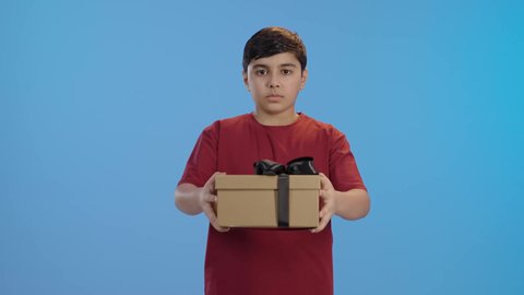 مناسبات وأعياد سعيدة،بورتريه لولد عربي خليجي سعودي مبتسم يرتدي الزي الكاجوال ينظر إلى الكاميرا يحمل بيديه علبة هدية مغلفة،  الشعور بالسعادة والفرح, مفهوم الموده والالفه ، تقديم الهدايا والتهنئات