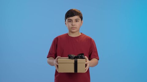 بورتريه لولد عربي خليجي سعودي مبتسم يرتدي الزي الكاجوال ينظر إلى الكاميرا يحمل بيديه علبة هدية مغلفة، مناسبات وأعياد سعيدة، الشعور بالسعادة والفرح, مفهوم الموده والالفه ، تقديم الهدايا والتهنئات