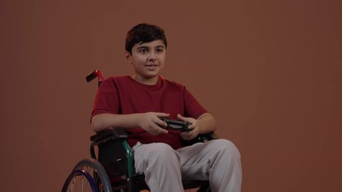 قضاء وقت ممتع في ألعاب الفيديو الترفيهيه، بورتريه لولد عربي خليجي سعودي يرتدي الزي الكاجوال يجلس على كرسي متحرك يحمل بيده عصا التحكم، إيماءات الاستمتاع والاندماج، استخدام جهاز تكنولوجي تقني حديث ومتطور